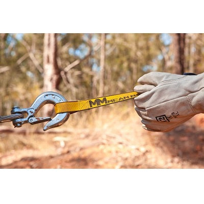 A person wearing protective gloves uses a Mean Mother 4x4 Snatch Strap 8,000kg Safety Bundle, featuring durable nylon webbing in yellow, which is attached to a metal hook and cable. The background displays a blurred outdoor scene with trees and dry vegetation.