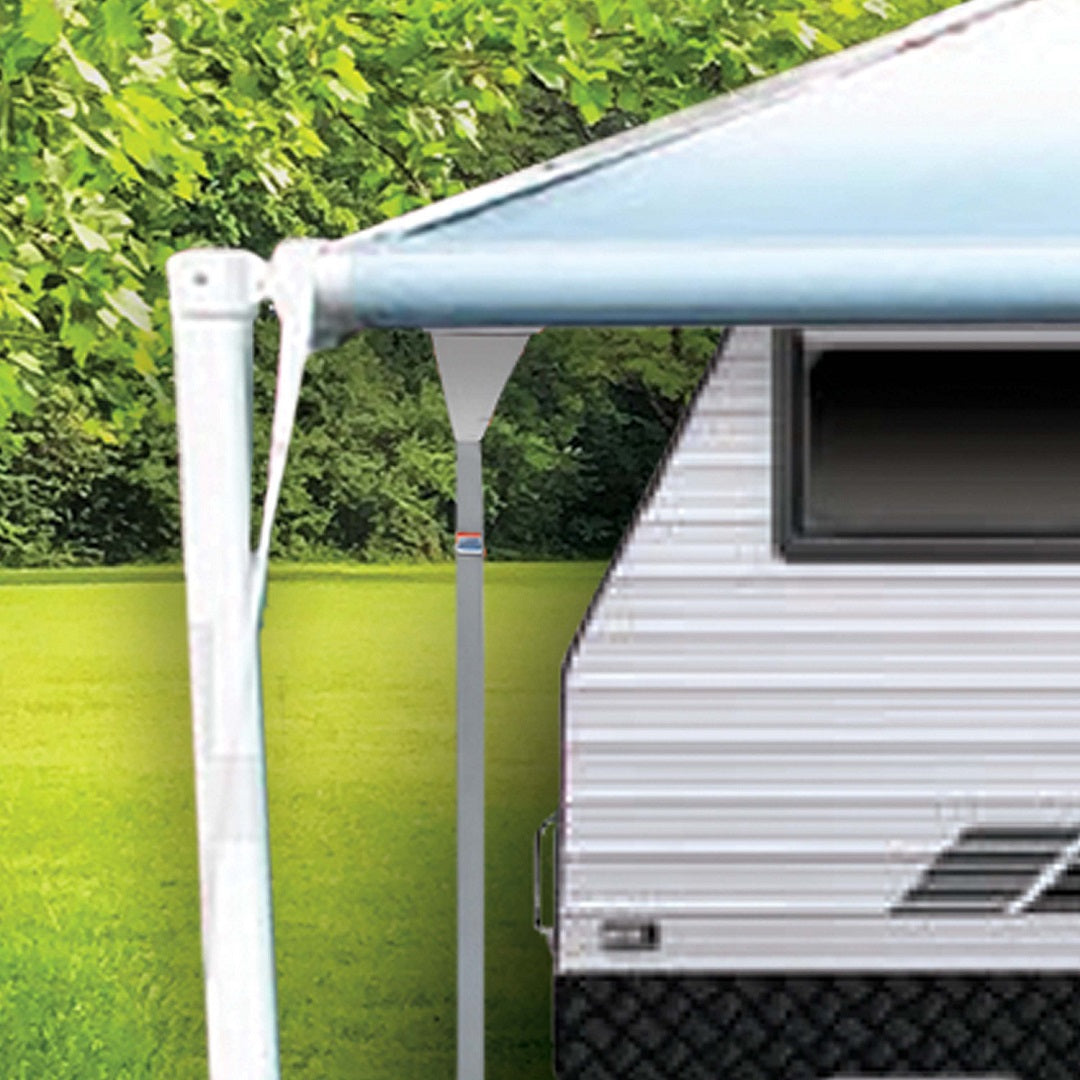 A close-up of the Explore Caravan Awning Tie-Down Kit attached to a recreational vehicle (RV) with green trees and grass visible in the background. The awning, enhanced with adjustable straps from the Explore brand for added stability, is extended to provide shade next to the RV, which has a gray and black design on its side.