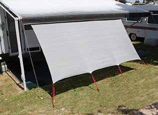 An Explore Caravan Privacy Screen, 1.8m x 4.9m, made with breathable mesh for UV reduction, is attached to a camper and extends over grass. Supported by four red poles, it offers comfort. A camper and another vehicle can be seen in the background.