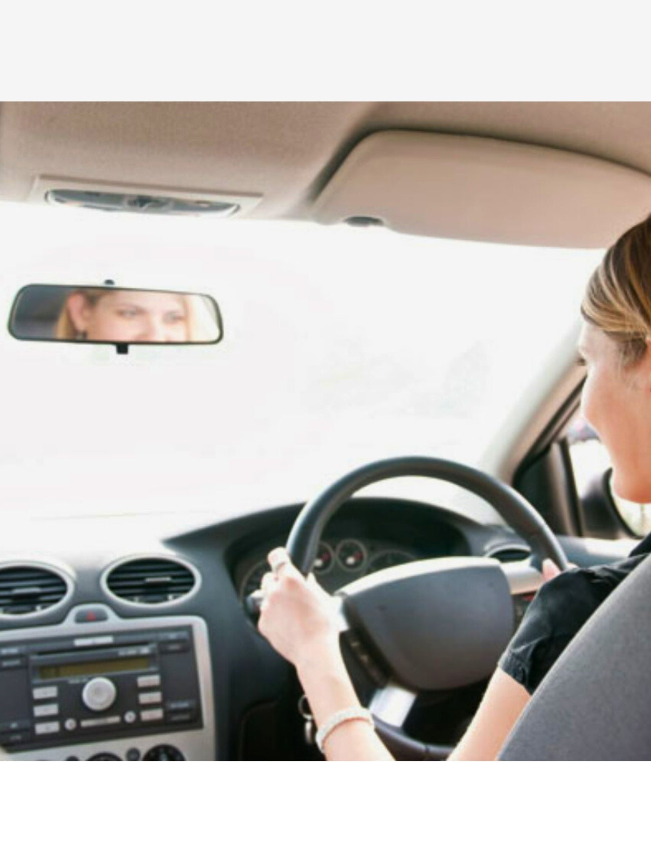 A person drives a car with a Sunland-Protection Mirror Rear View - Day/Night Universal, minimizing glare. The interior showcases a dashboard with a universal mounting control panel and the steering wheel.