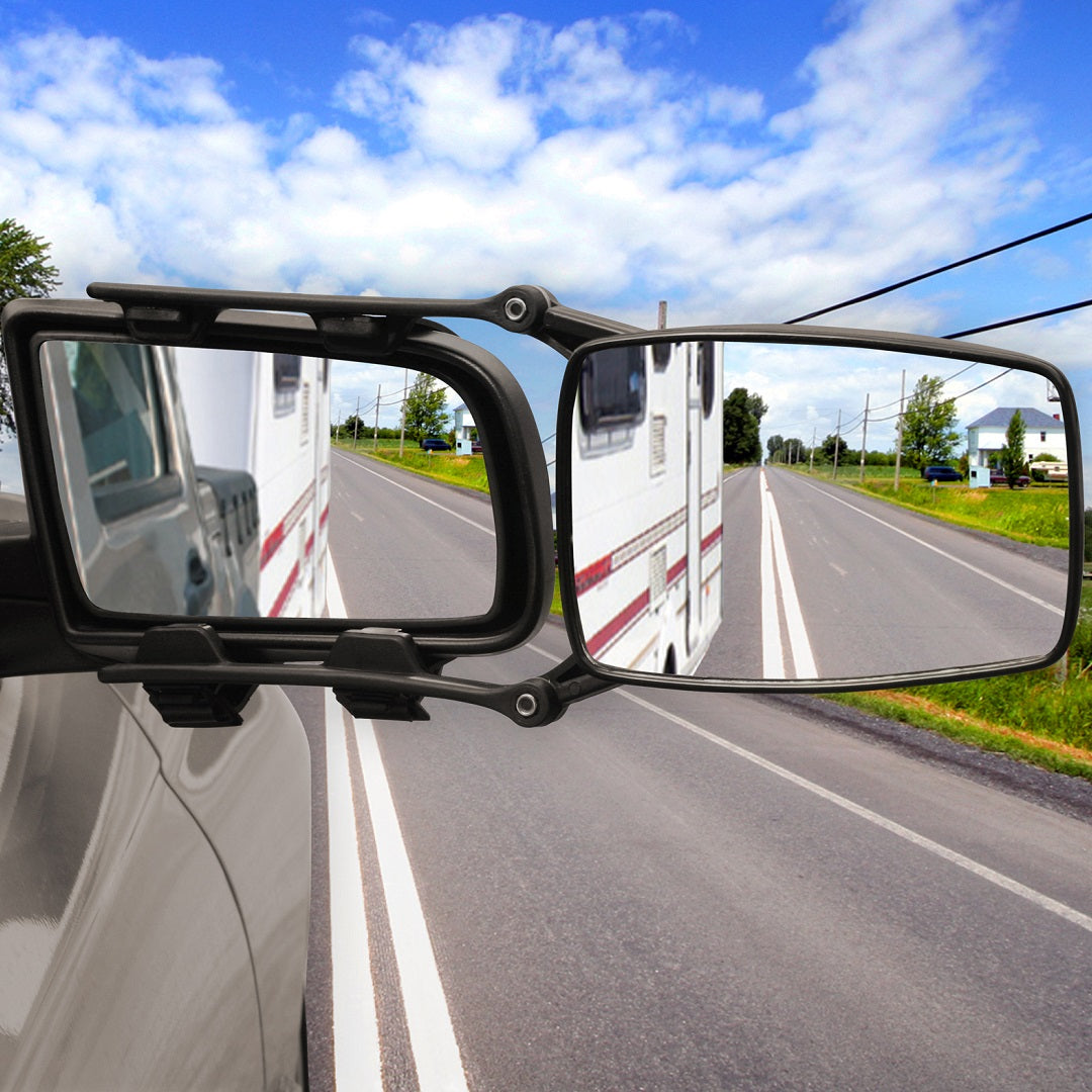The Drive Towing Mirror Large, a universal towing mirror, reflects an RV adorned with red stripes. The road ahead is unobstructed, bordered by grass and power lines beneath a blue sky dotted with clouds.