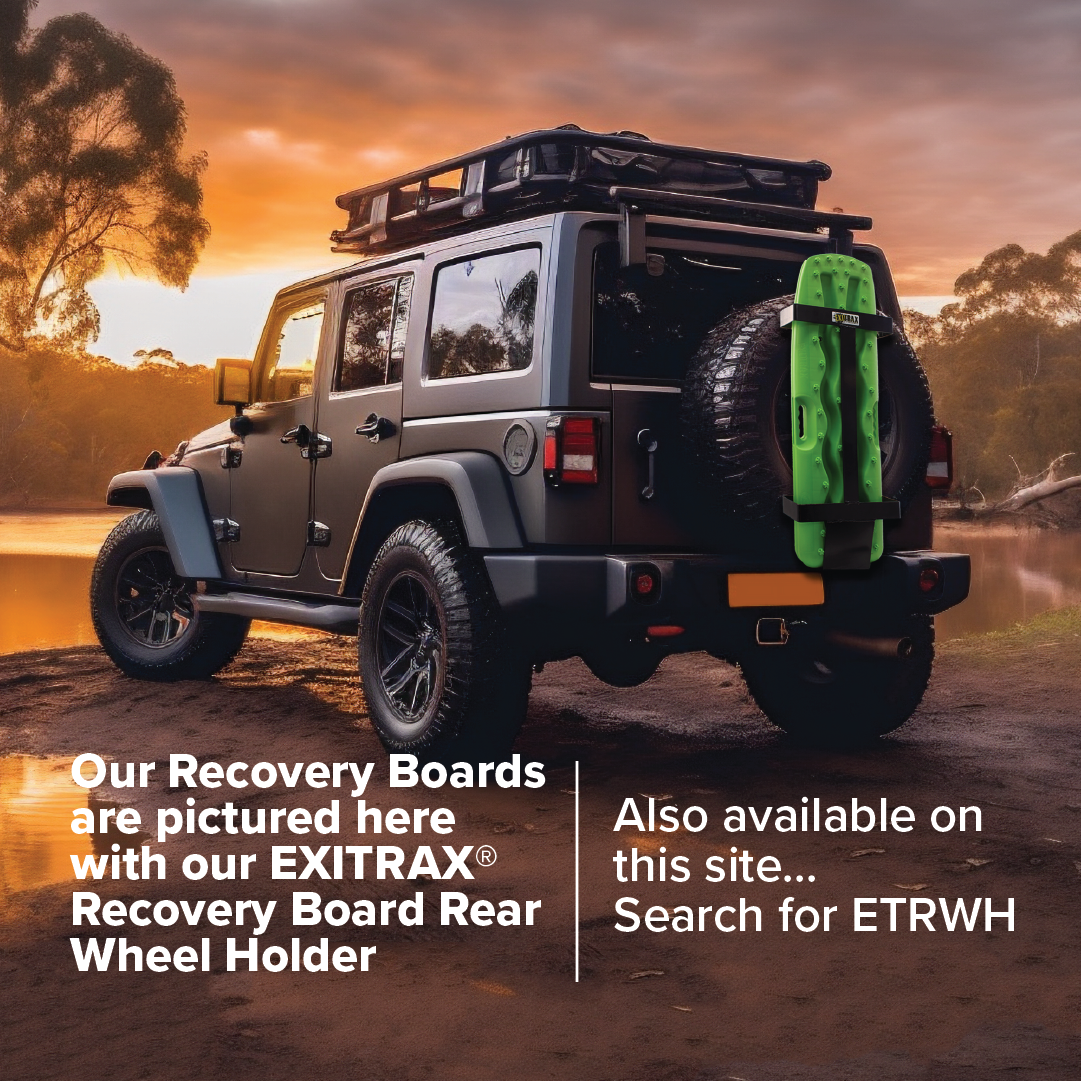 A black Exitrax Recovery Board 930 Series is mounted on the rear of a rugged off-road vehicle, which also features a rooftop rack and spare tire. The stunning sunset by the lake serves as a backdrop, highlighting the unparalleled traction and lifetime warranty offered by the EXITRAX Recovery Board Rear Wheel Holder.