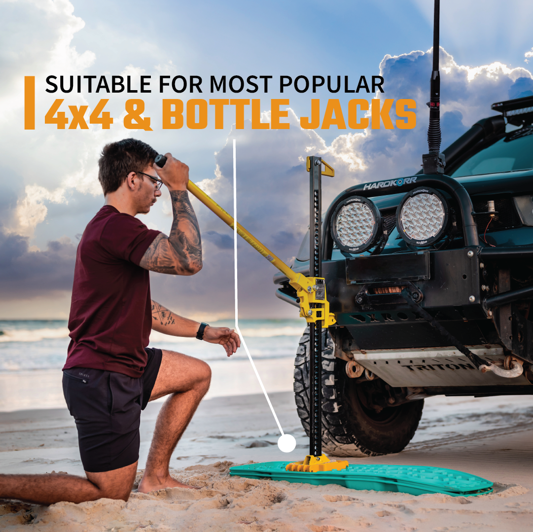 A man uses an Exitrax Exilink Recovery Boards Link Plate / 4WD Jack Base to lift a black 4x4 on a sandy beach at sunset. Bold text reads, “Suitable for most popular 4x4 & bottle jacks.”.