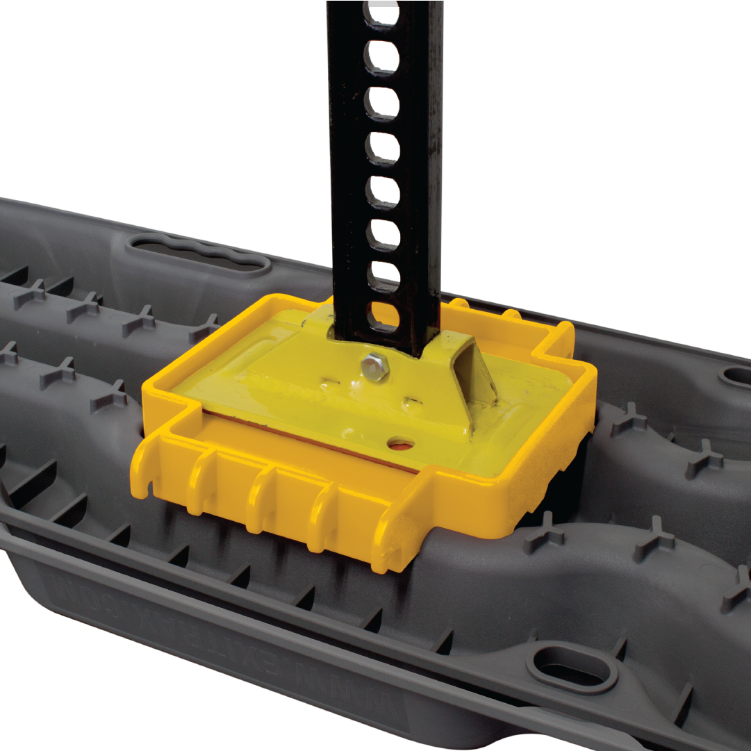 A close-up of the Exitrax Recovery Board Link Plate / Jack Base | Exilink, showcasing its yellow and black automotive jack, mounted on a flat, textured black base with a grooved surface. The yellow component secures the vertical black metal bar, which features evenly spaced holes along its length. This setup pairs well with the Exitrax Ultimate Series recovery boards for off-road adventures.