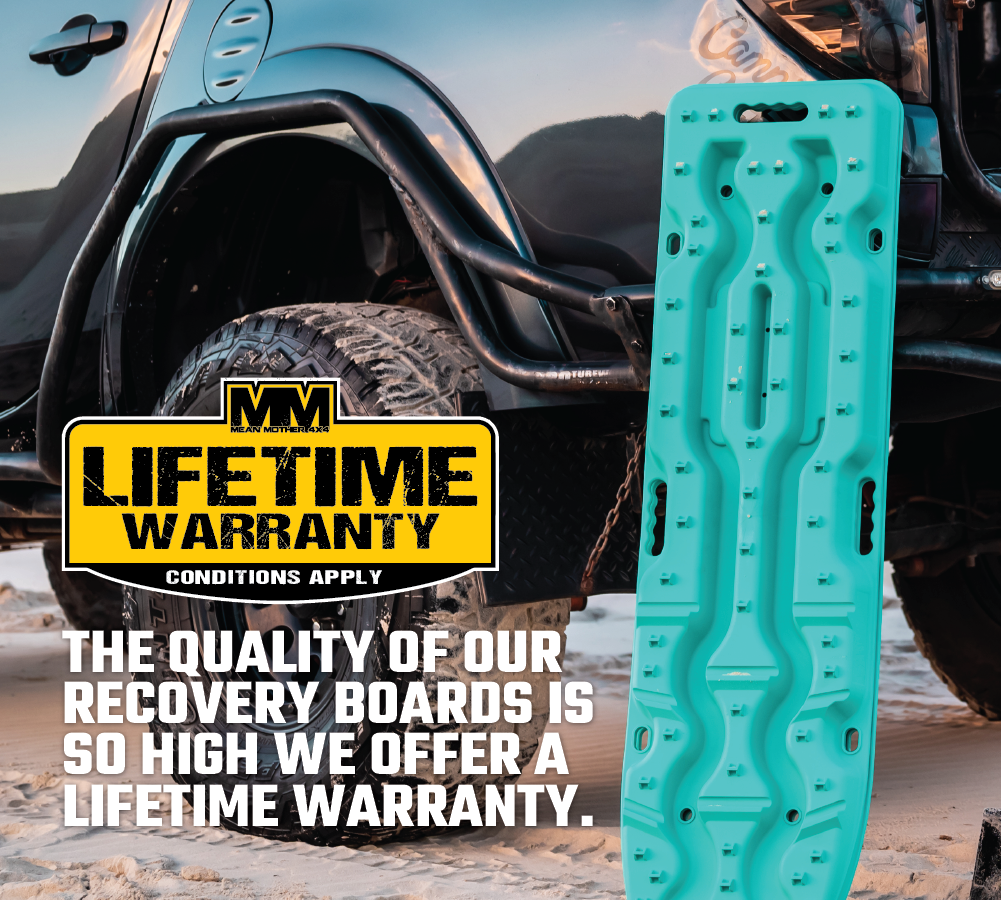 An Exitrax Recovery Boards Ultimate 1150 - Aqua Marine stands upright in sand beside an off-road vehicle. Overlay text: "Our recovery boards are so high quality, we offer a lifetime warranty.*" *Conditions apply.