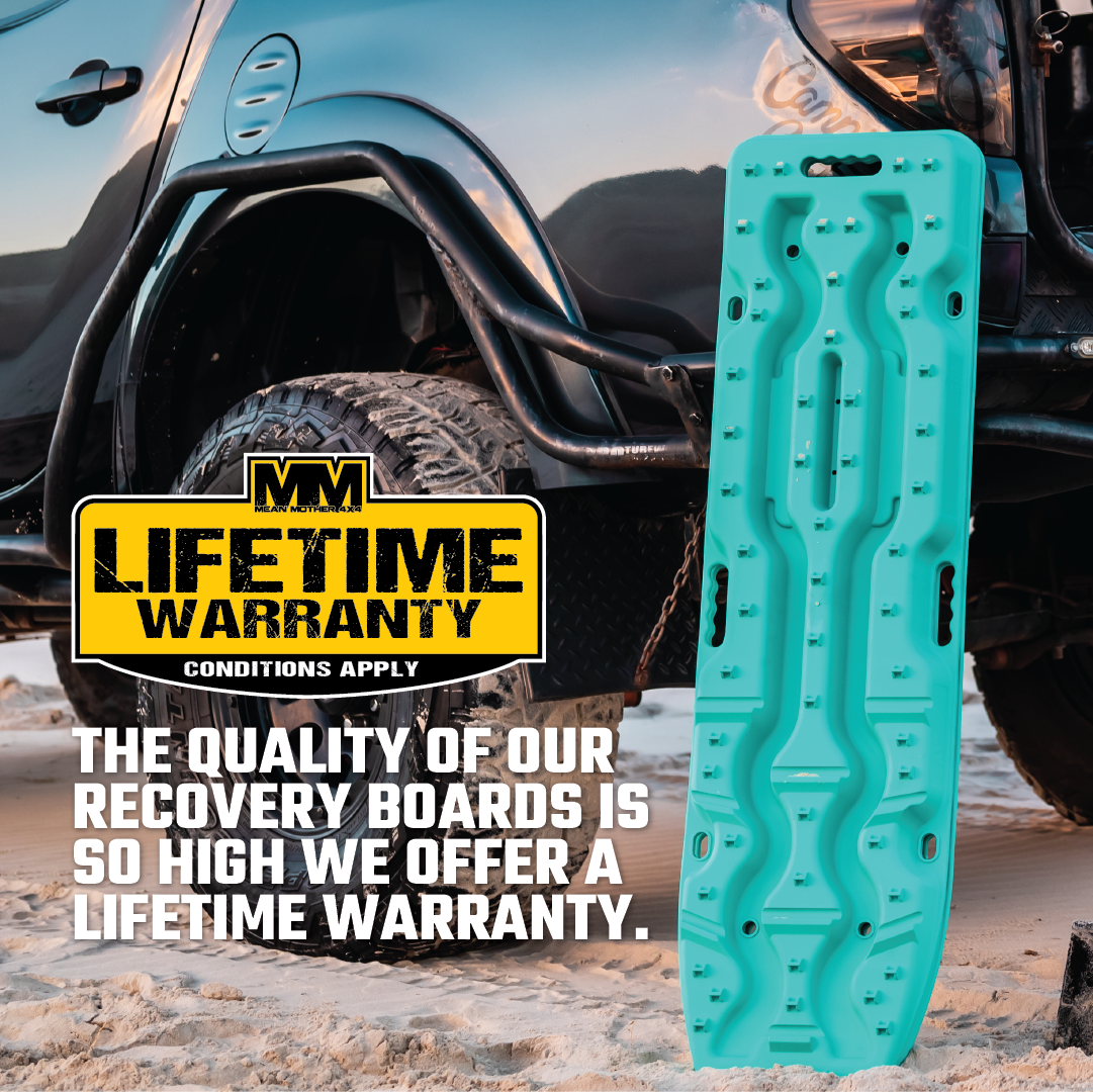 A black Exitrax Recovery Boards Ultimate 1150 + FREE Tyre Deflator Bundle stands upright before an off-road vehicle on sand. The image features a lifetime warranty, showing the durability of these essential 4x4 recovery boards.
