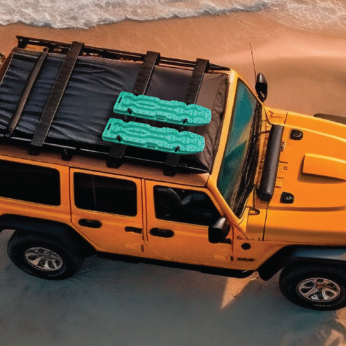 A yellow 4x4 is parked on a sandy beach near the water, with two Exitrax Recovery Boards Ultimate 1150 in Blood Orange secured to its roof rack.
