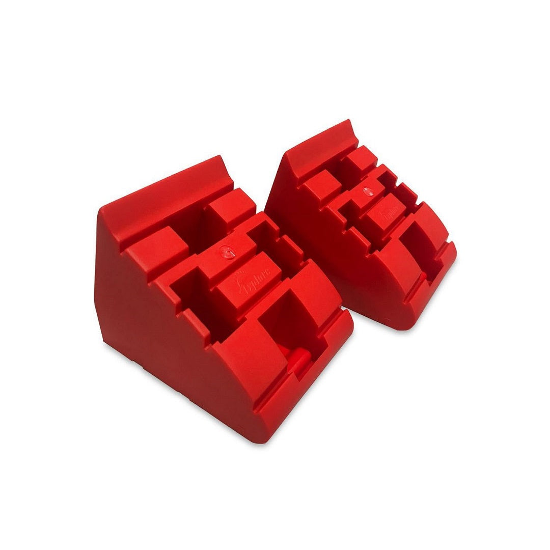 Two red, triangular Explore Caravan Levelling Ramp Chocks stand side by side, featuring a ridged surface for added grip. These chocks prevent vehicle movement effectively, with their vivid color enhancing visibility and signifying quality craftsmanship.