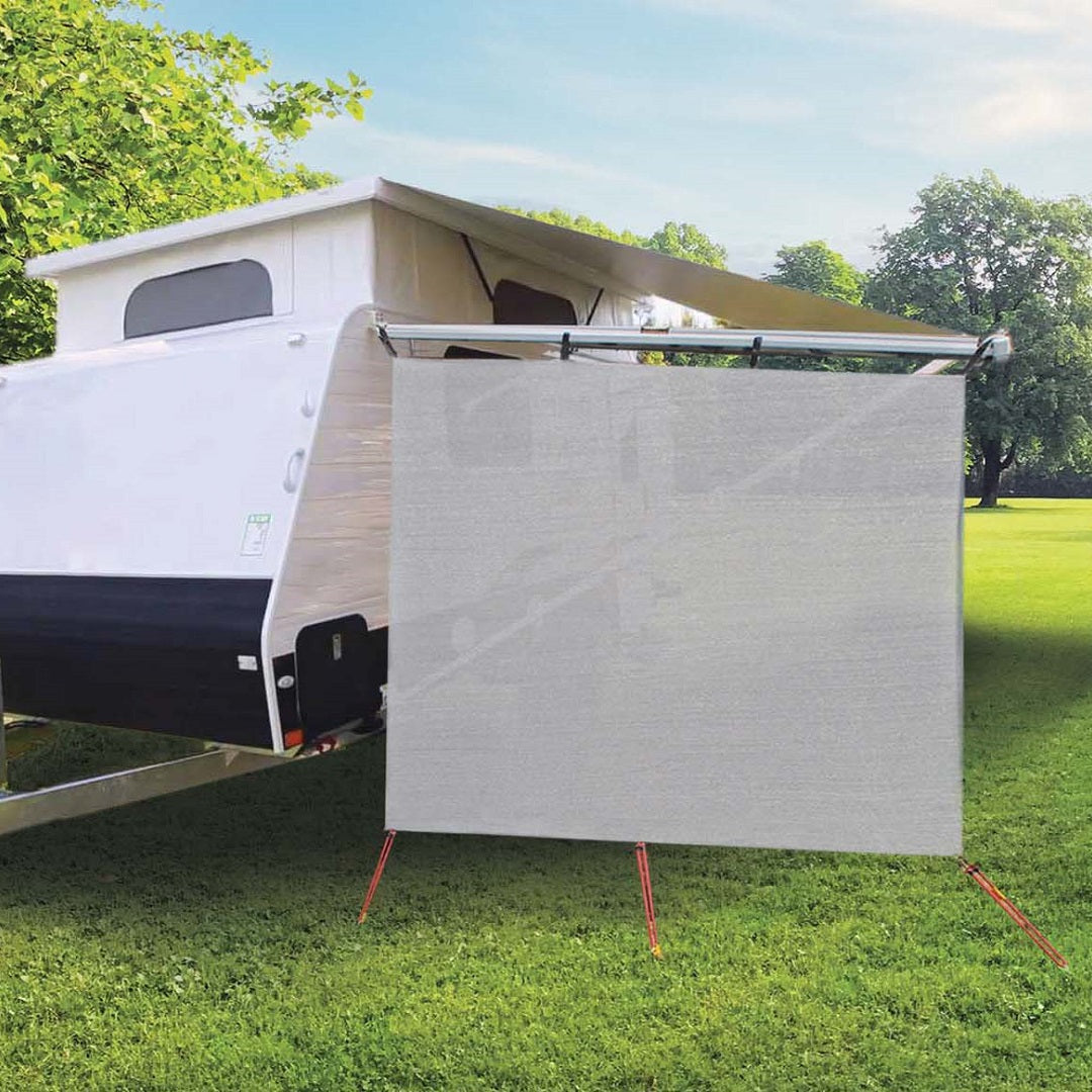 An Explore Caravan Pop Top has its Explore Caravan Pop Top End Privacy Screen attached, offering ample shade and added seclusion or sun protection. The caravan is parked on a grassy area surrounded by trees and greenery.