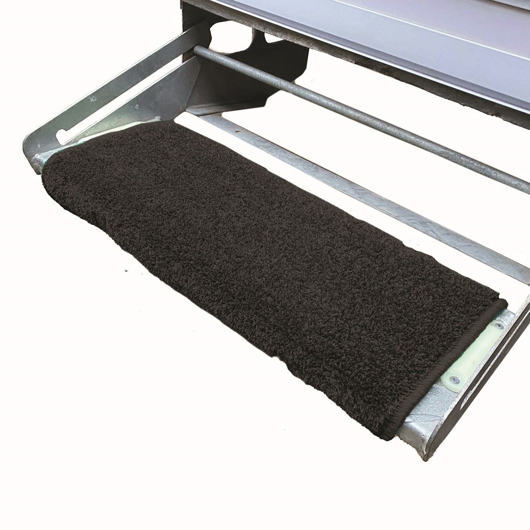 The Explore Caravan Step Mat - Black, a dark rectangular mat made of non-slip material, covers a metal step that seems to be part of a larger structure, likely a vehicle or piece of equipment. The metal frame and rods provide support for the step, ensuring it is sturdy enough to keep your caravan floor clean.