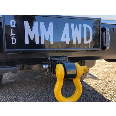 A detailed image showcasing the Mean Mother Recovery Hitch / Shackle on a vehicle's rear hitch receiver, featuring a yellow tow hook and bow shackle. The license plate displays "QLD MM 4WD," with a blurred outdoor background providing context.