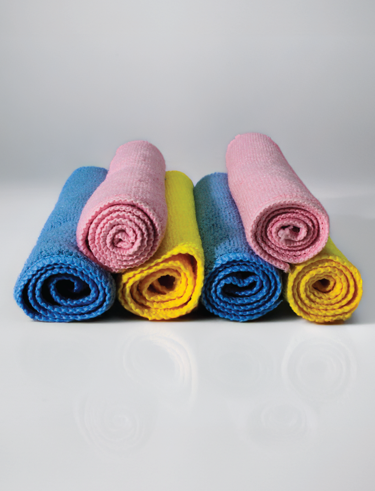The Sunland-Protection Ultra-soft Microfibre 6 x Towel Pack forms a pyramid on a reflective surface. The top row features two pink towels, while the bottom has two blue and two yellow ones. Their high-density weave ensures each towel is lint and streak-free against the smooth, light gray background.