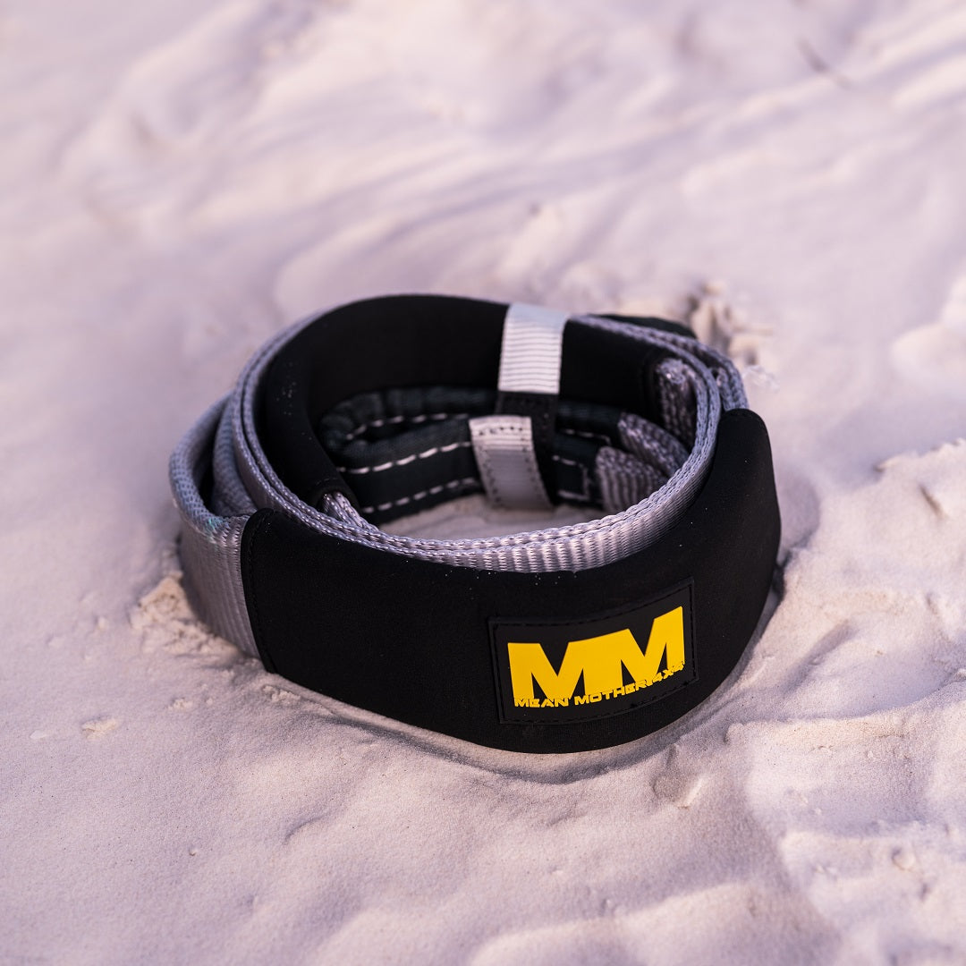 A coiled Mean Mother Equaliser Strap 75mm / 2.5m 8,000kg (Trade Show Only) with a yellow MM logo rests on white sand.