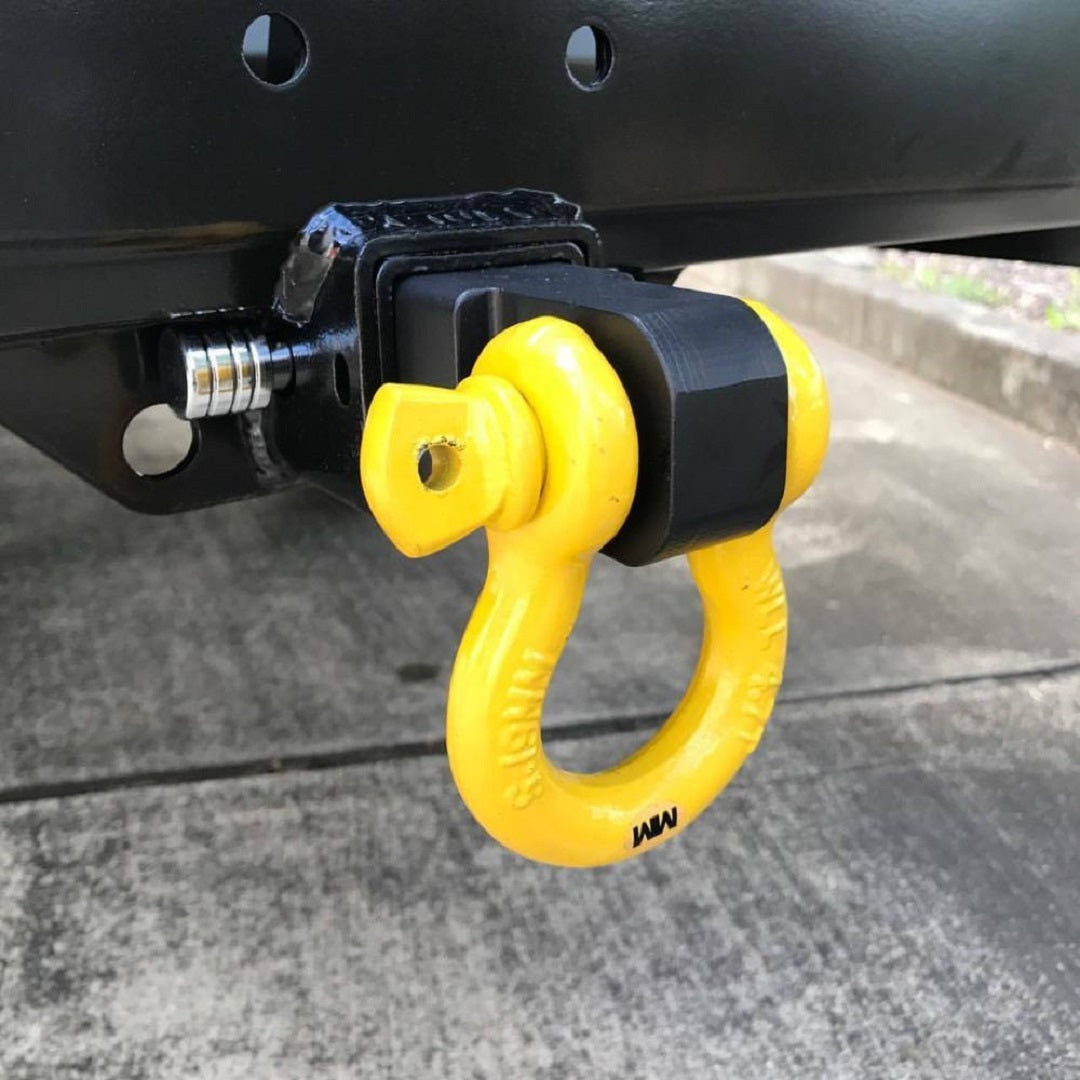 Close-up of the Mean Mother Recovery Hitch / Shackle featuring a yellow bow shackle connected to a black hitch receiver. The towing system is securely attached and ready for use, set against a concrete surface.