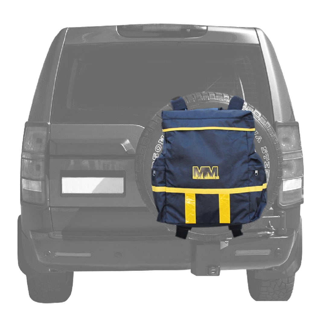 A mid-sized backpack with yellow accents is positioned against the Mean Mother 4x4 Rear Wheel Bag of a black SUV. The vehicle’s spare tire peeks out, while the heavy-duty bag prominently features a yellow "MM" logo on its back.