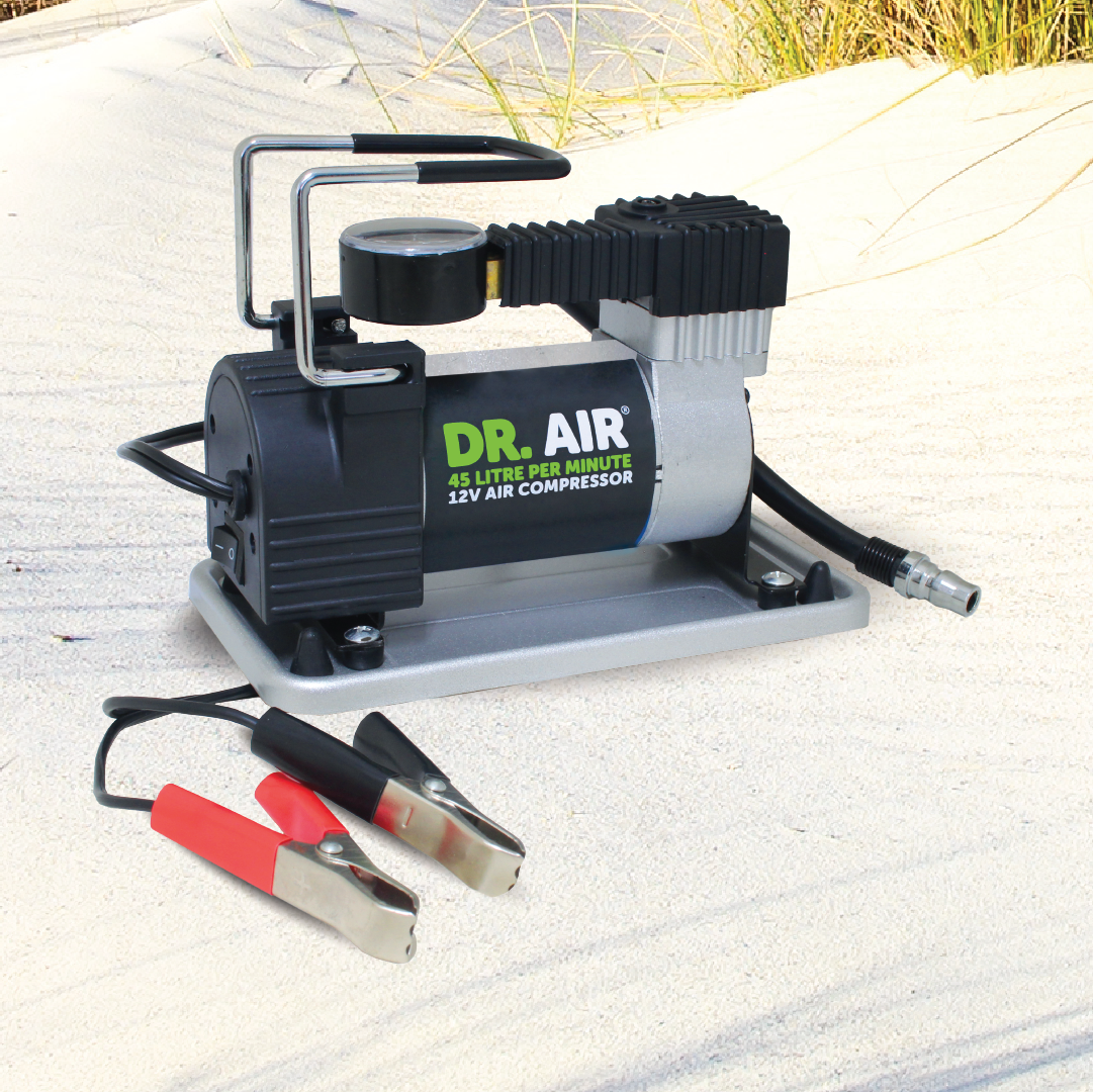 A compact air compressor from Dr Air, named the 12V Air Compressor 45 Lpm, is positioned on sandy terrain. It offers an impressive air delivery rate of 45 liters per minute at 12 volts. Equipped with a pressure gauge and attached cables, it serves as a dependable option for various inflating tasks.