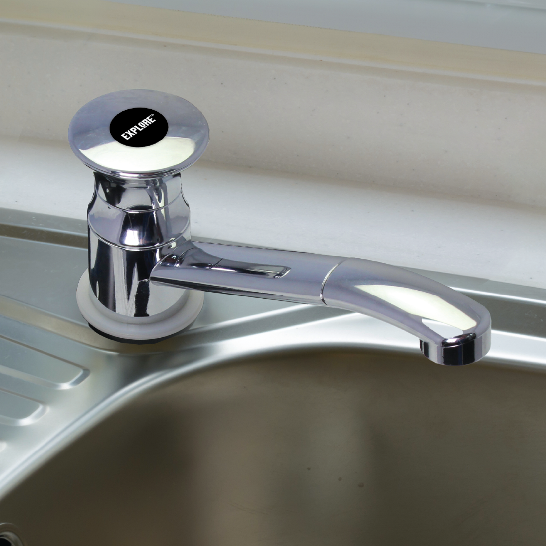 The Explore RV Sink Hand Pump - Chrome is mounted on a steel sink, perfect for caravans or camper trailers. The faucet features a round knob at the base labeled "EXPLORE" in black with white text. The sink has a drainer area with ridges on the left side, making it ideal for outdoor wash stations.