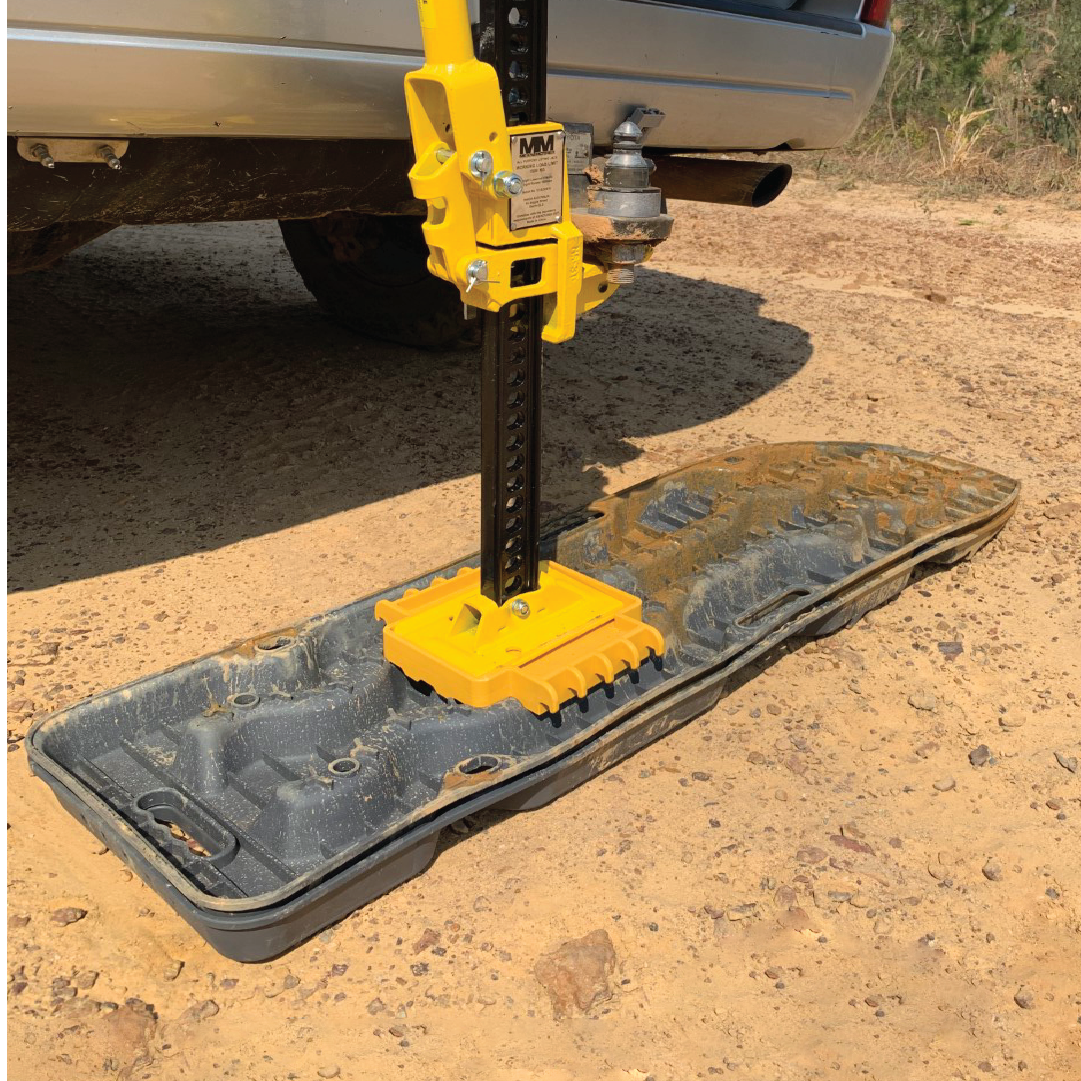 The Mean Mother High Lift Jack 48" secures a vehicle's rear, positioned on a black traction board over sandy terrain. This yellow lifting mechanism by Mean Mother features a handle for manual operation and is an essential part of recovery accessories.