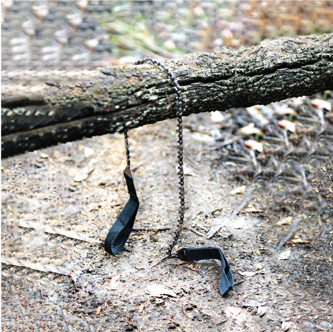 The Mean Mother Pocket Chain Saw by Mean Mother 4x4, featuring two black handles, rests over a moss-covered fallen tree log on the forest floor. This efficient wood-cutting tool integrates perfectly into the natural woodland environment, surrounded by leaves and twigs that provide an ideal backdrop for essential camping gear.