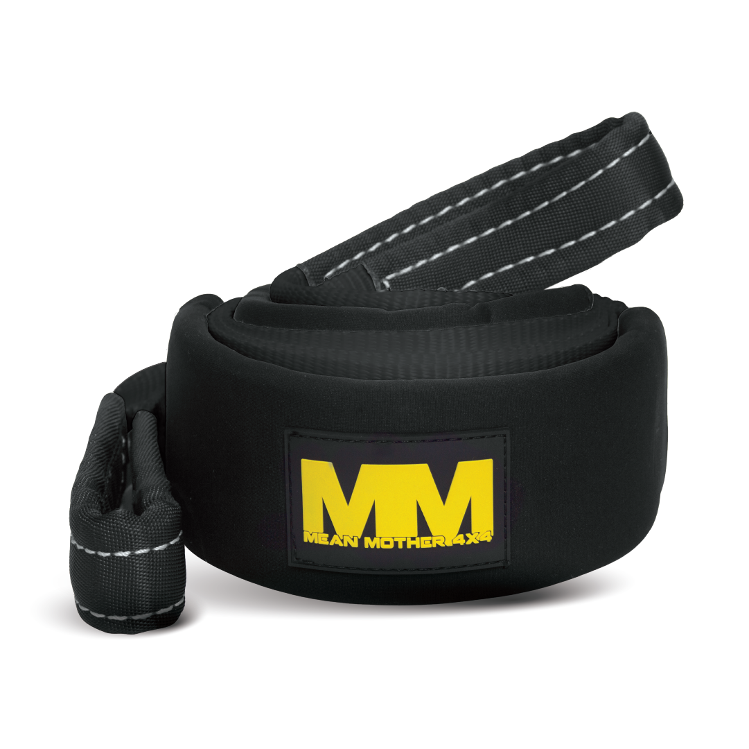 The Mean Mother Tree Trunk Protector, measuring 75mm x 3m and capable of withstanding up to 12,000kg, is a robust black tow strap featuring reinforced stitching and a looped end. It doubles as a trustworthy tree trunk protector and prominently displays a black patch with the yellow "MM" logo and "Mean Mother" text.