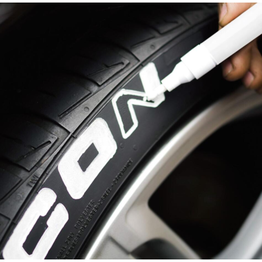 A hand uses the Drive Tyre Paint Marker to highlight embossed letters on a black car tire with a silver alloy wheel, creating a striking contrast reminiscent of classic white walls.