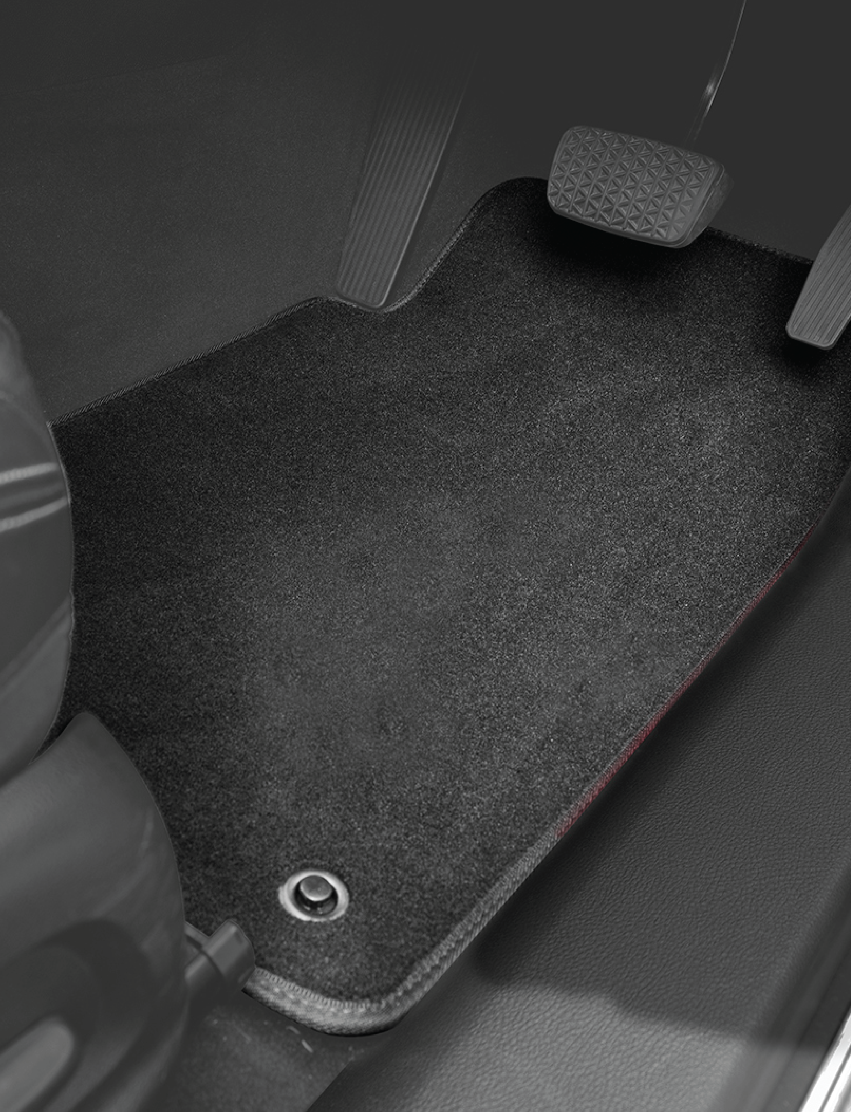A close-up view of the driver's side footwell area featuring a luxurious, black carpeted Sunland-Protection Tailored Floor Mat for the Mazda 3 (2009-2014). The brake and accelerator pedals are visible above this durable premium mat, which fits the space precisely and includes a round securing ring in the bottom left corner.