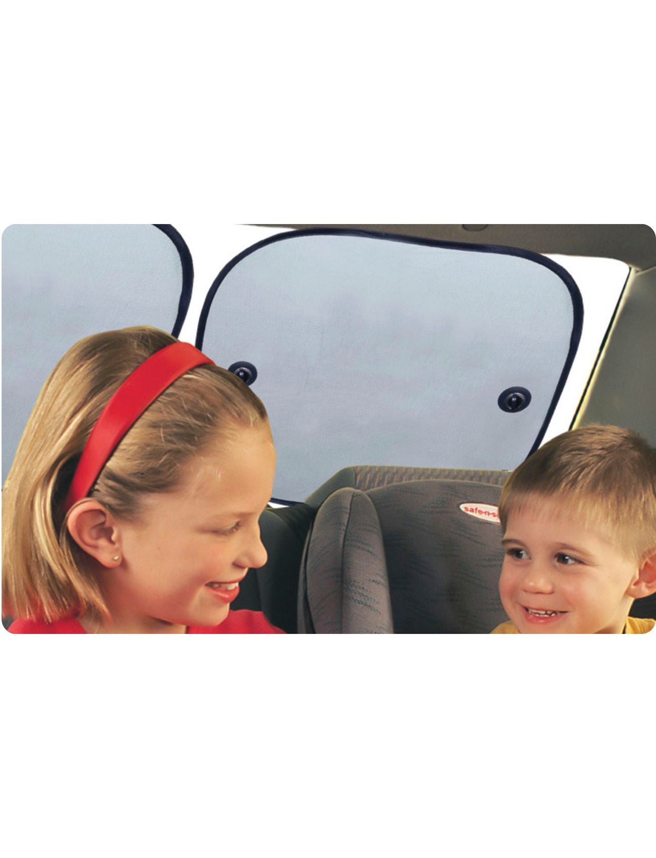 Two young children smile at each other in the back seat. The older child wears a red headband, and the younger is securely seated in a gray car seat. Sunland-Protection Car Sun Shades cover the rear windows, casting gentle shadows over their cheerful faces.