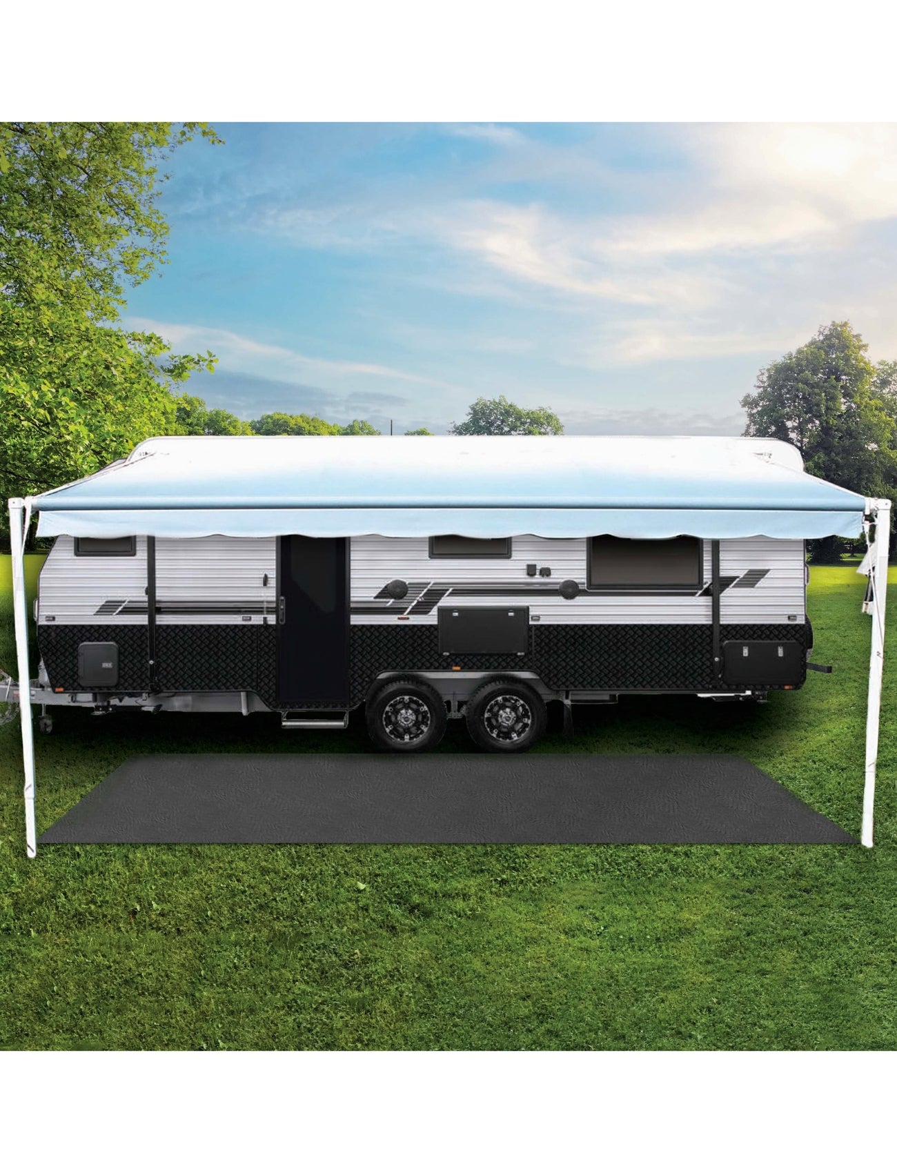 A travel trailer is parked on lush green grass, with its awning made from the Sunland-Protection Caravan Annexe & Floor Matting 2.5 x 6m, featuring UV-stabilized open weave mesh for optimal shade. The clear sky hosts a few clouds, and trees stand tall in the background, completing this peaceful outdoor setting.