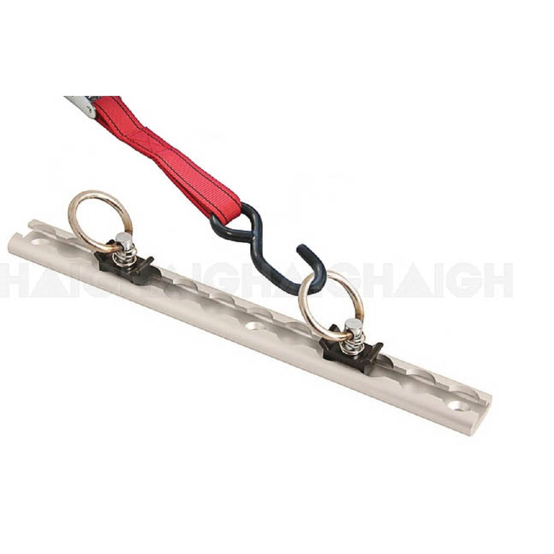 The Cargo Mate Tie Down Anchor Tracks - 30cm by Cargo Mate is an aluminum alloy metal tie-down bar with adjustable anchor points, featuring multiple holes and two ring anchors secured by bolts. A red strap is hooked onto one of the rings, held in place by a black hook, against a plain white background.