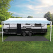 An Explore Caravan & Floor Matting 2.5 x 3m with a sleek mesh design and extended awning is parked on a grassy area. The dual-axle trailer, equipped with slip-resistant steps, blends beautifully with the lush green landscape beneath a partly cloudy sky.