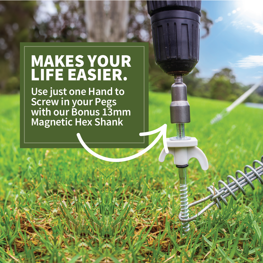 A close-up of the Explore cordless drill driving an Explore Hard Surface Metal Screw Peg into the ground using the included 13mm magnetic hex shank. The grassy field in the background is slightly blurred, and a text overlay reads, "MAKES YOUR LIFE EASIER. Use just one Hand to Screw in your Pegs with our Bonus 13mm Magnetic Hex Shank.