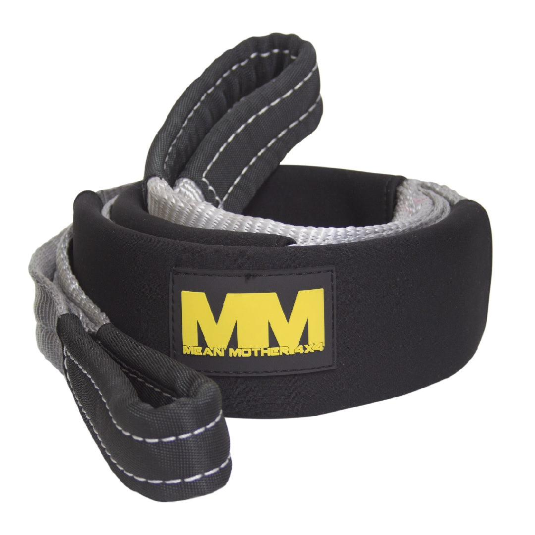 A black and silver Mean Mother Equaliser Strap, measuring 75mm in width and 2.5m in length, is coiled neatly. This robust 8,000kg recovery strap features reinforced loops at both ends and bears a patch in the middle with bold yellow lettering that reads "MM MEAN MOTHER 4X4". Visible stitching along the edges enhances durability, while a protective sleeve adds an extra layer of resilience.