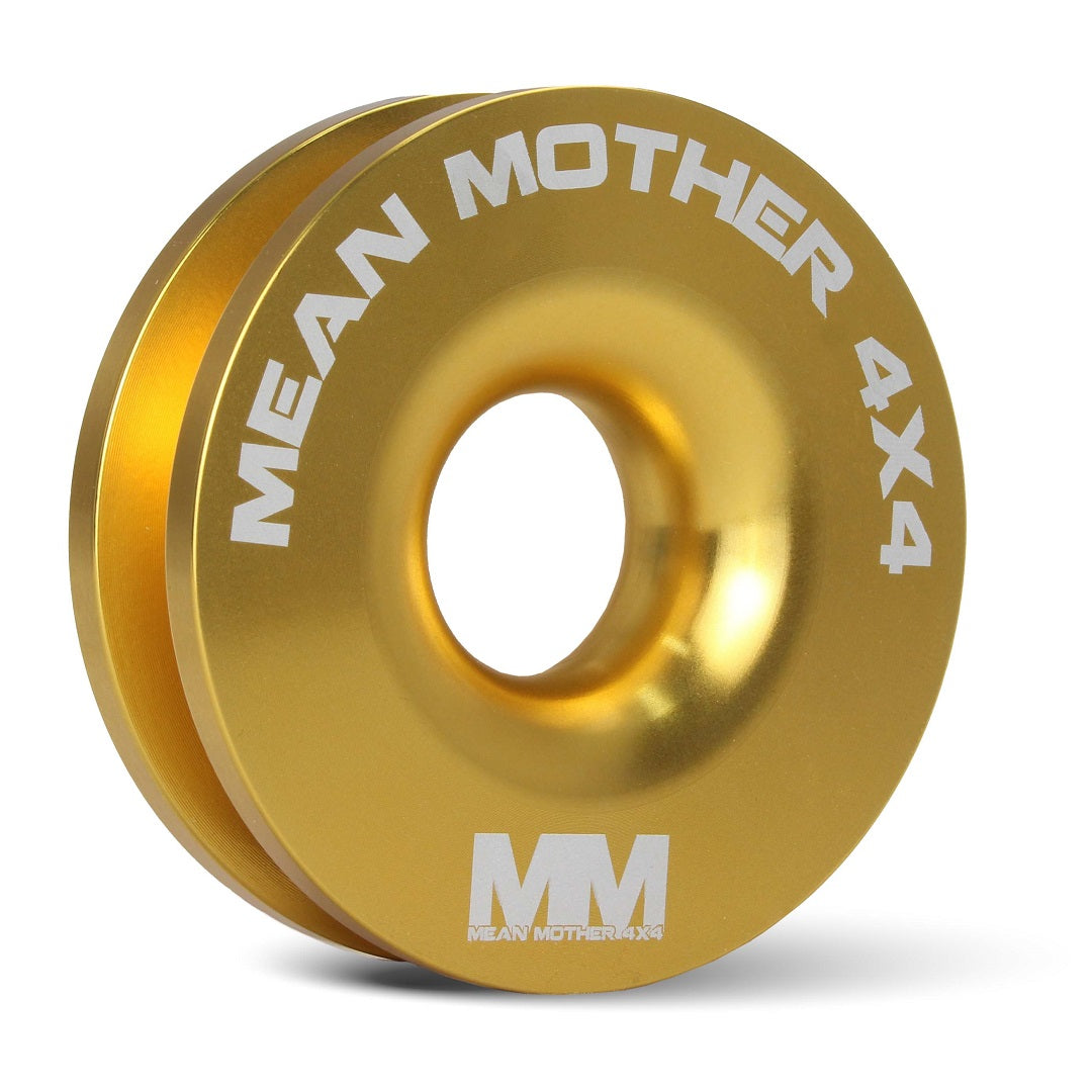 A circular gold snatch ring from the "Soft Shackle & Snatch Ring Bundle" by Mean Mother 4x4, featuring the "MM" brand logo at the bottom and "Mean Mother 4x4" in white lettering along the edge. It includes a central hole and v-groove, making it ideal for use with UHMPE synthetic rope or a soft shackle, perfect for a 4x4 Recovery Kit.