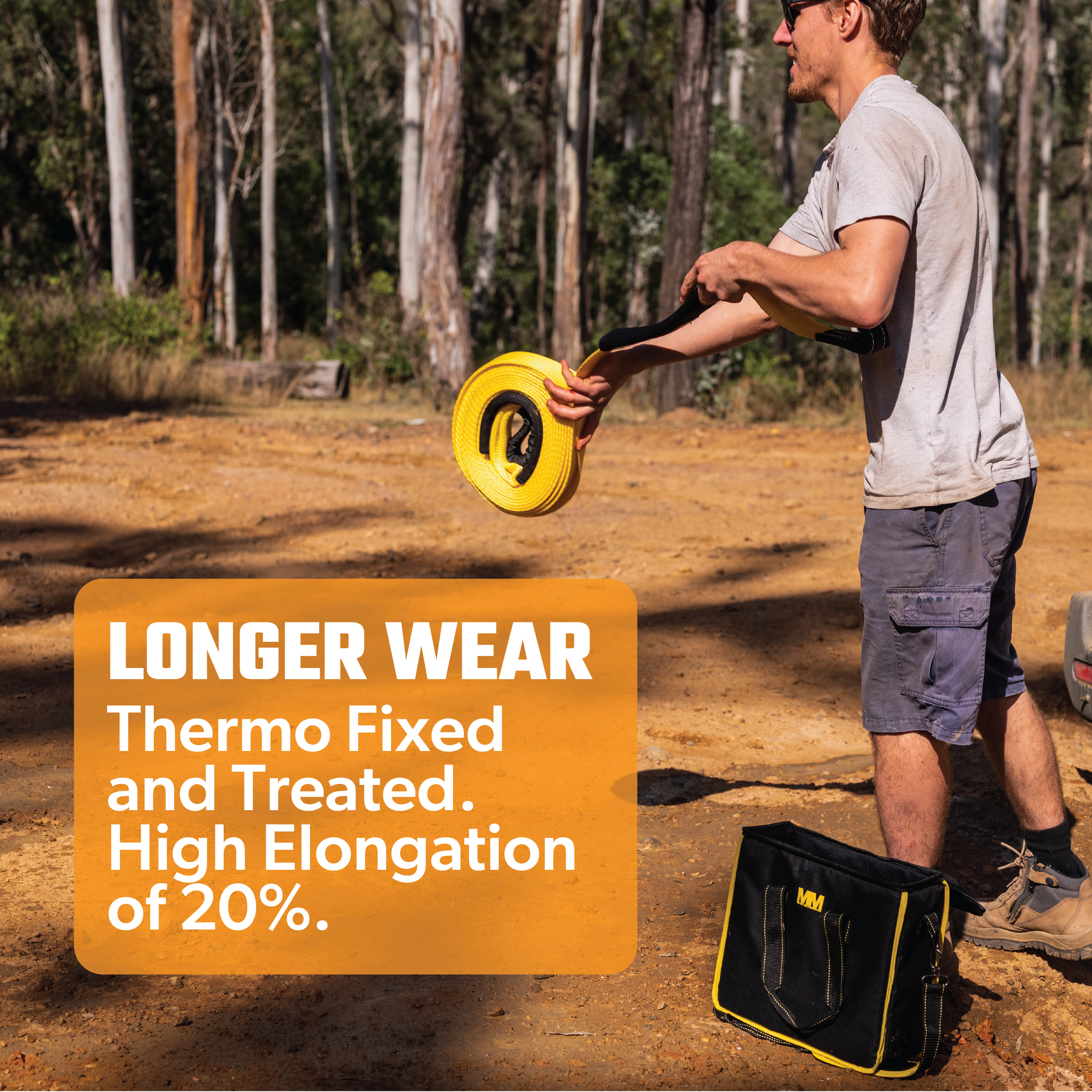 A person stands on a dirt path surrounded by trees, holding a yellow Mean Mother Snatch Strap 8,000kg. Text on the image reads: "LONGER WEAR, Thermo Fixed and Treated. High Elongation of 20%." Crafted from high tenacity nylon webbing, it promises durability. A black bag rests on the ground nearby.