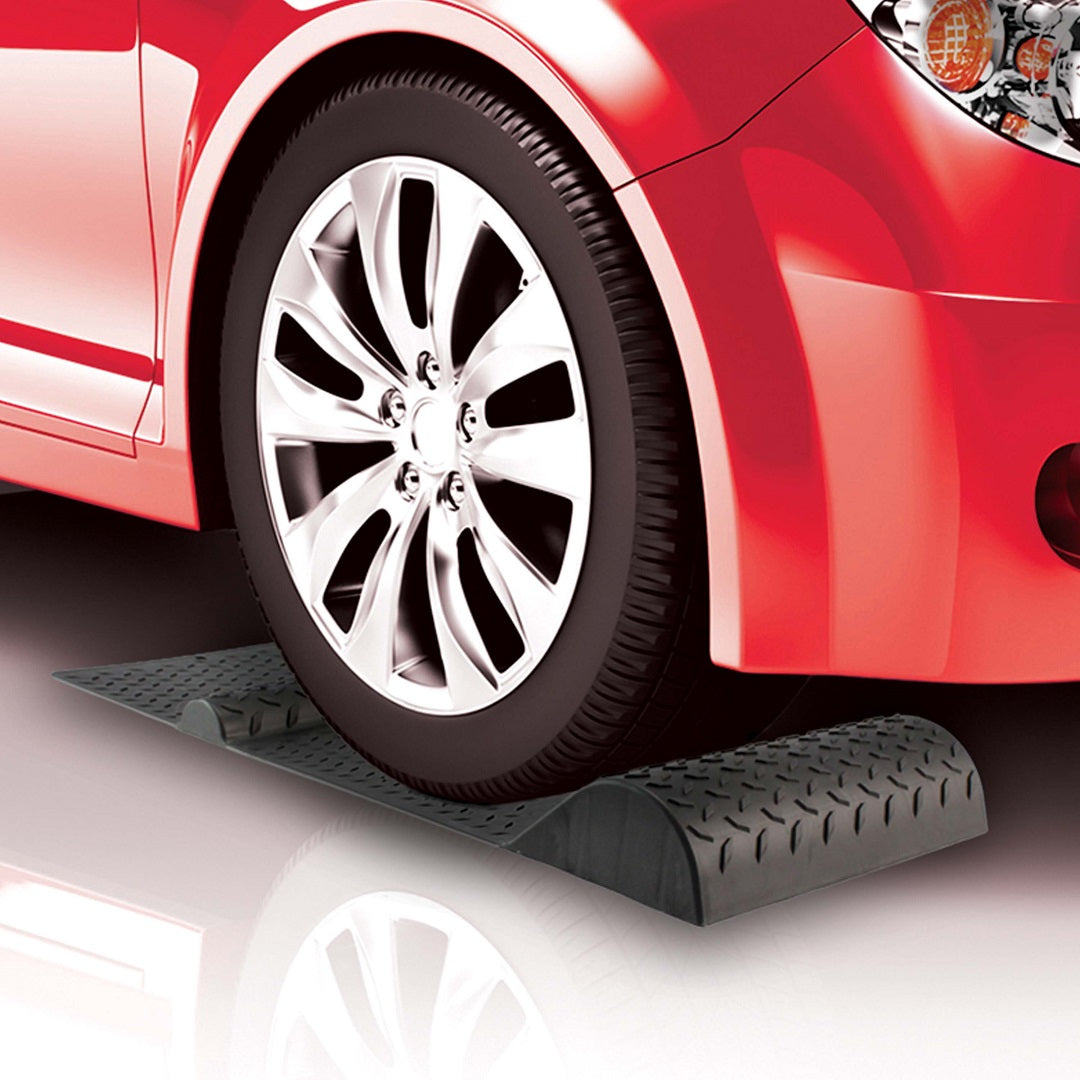 A red car with chrome wheels is parked on a set of Drive Parking Mats Wheel Stops. The textured black ramps serve as an excellent car storage solution. The front tire is lifted slightly off the ground by the ramp, showcasing how these Drive ramps function for maintenance or tire changes.