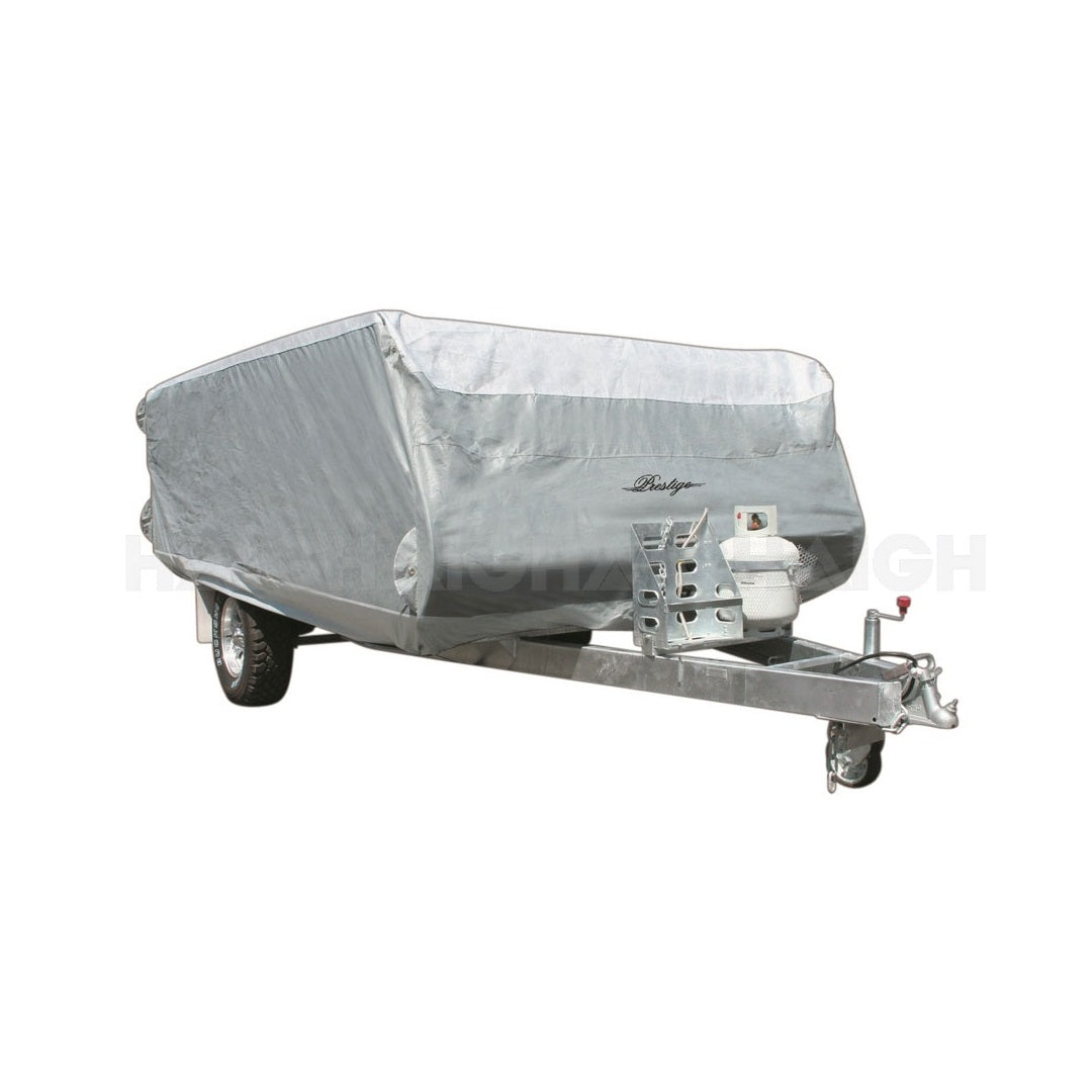 The Prestige Caravan Cover UP TO 2.43m features a silver UV-stabilised, waterproof fabric, showcasing the trailer's hitch and a propane tank attached at the front. It is supported on single axle wheels and includes a Pop Top Cover for added convenience.