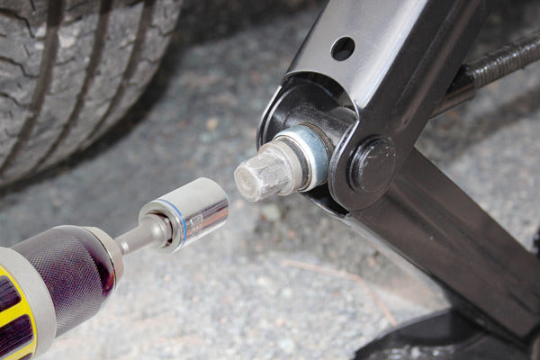 A close-up image displays a car tire being removed with a socket wrench connected to a power drill, while an Explore Caravan Jack supports the vehicle. The partially unscrewed bolt near the wheel illustrates precision and efficiency in action.