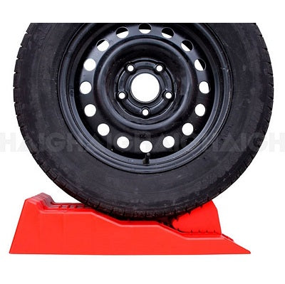 A black car tire mounted on a steel wheel is securely placed on the bright red Explore Caravan Levelling Ramp - Australian Made by Explore. This UV-resistant ramp provides a sturdy platform designed to elevate and stabilize the tire for maintenance or storage purposes, making it ideal for use as caravan or motorhome levellers.