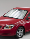 A red car is outfitted with a Sunland-Protection Interior Sun Shade, measuring 130cm by 60cm in silver, stretched across the front windshield to block UV rays. The image captures an angled view, highlighting part of the hood and left headlight against a plain, neutral background.